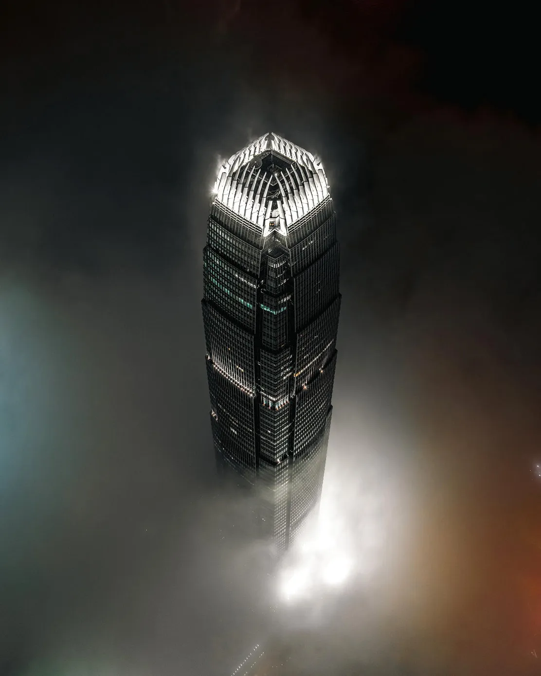 夜晚的香港摩天大楼从低云中探出,楼顶灯光在深色天空和雾气之间格外醒目