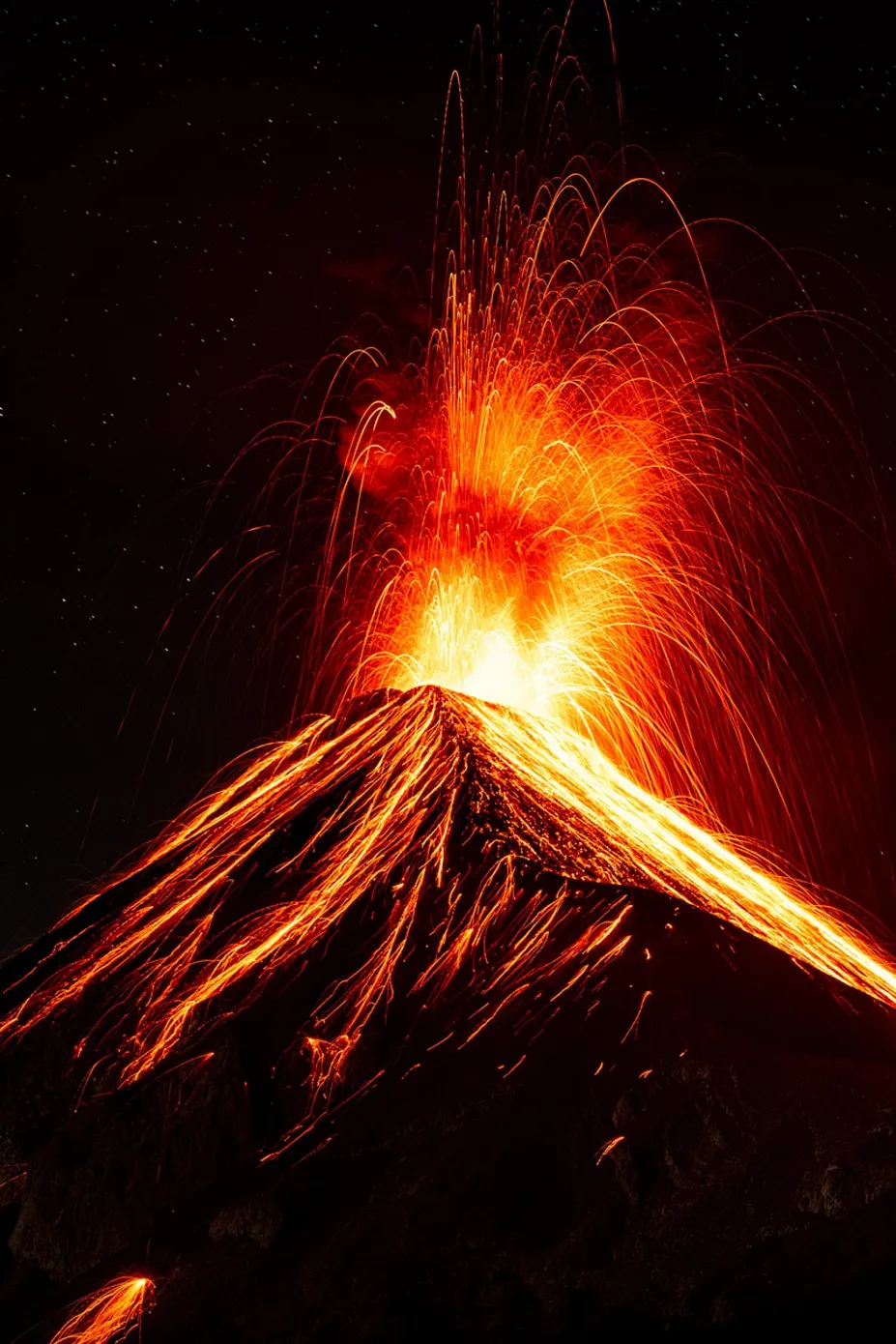 夜间喷发的富埃戈火山向天空喷出橙红色熔岩,炽热熔岩沿黑色山坡流下。