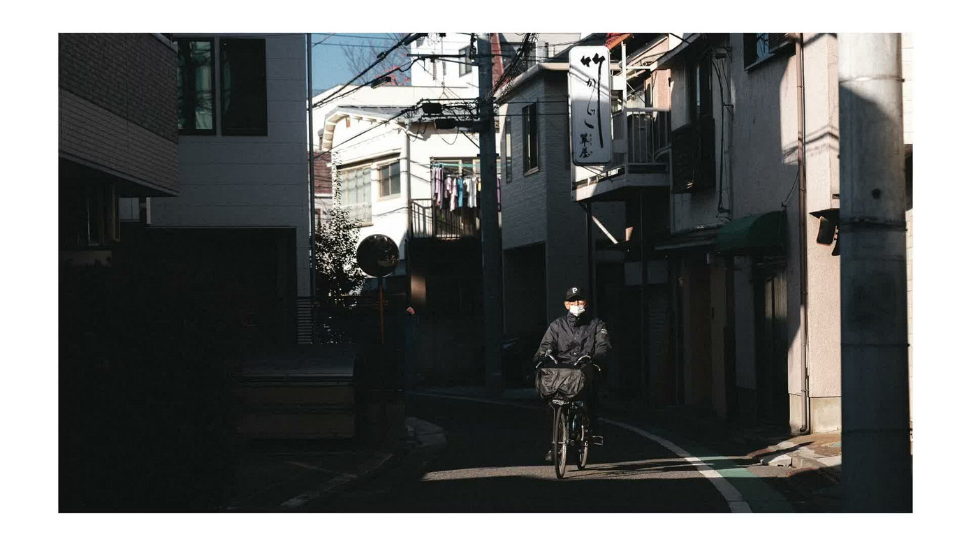 主体进入亮区后，街巷里的杂物被暗部弱化，观众会先看见骑车人
