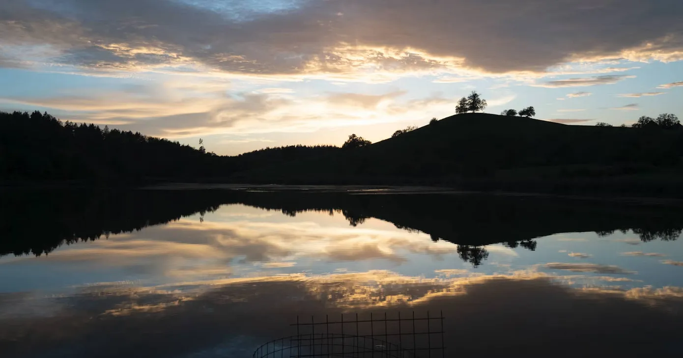 调色完成后的日落湖面,橙红色云层倒映在平静湖水中,远山与岸边树木呈剪影